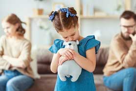 Child holding a teddybear with fighting parents sitting at oppposite ends of sofa in background